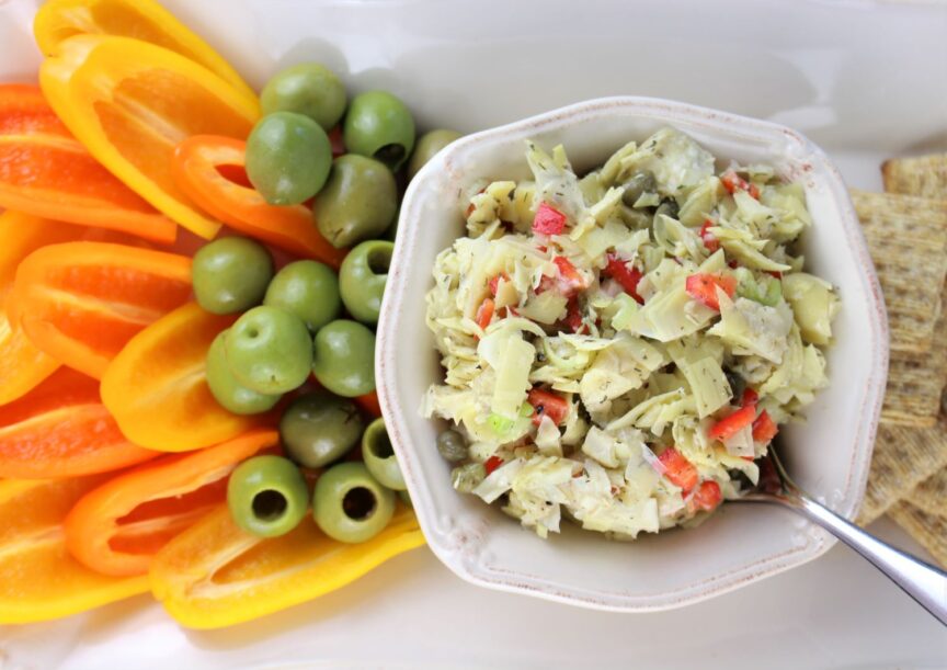 Chunky artichoke dip served with orange and yellow mini bell peppers halved and castelvetrano olives