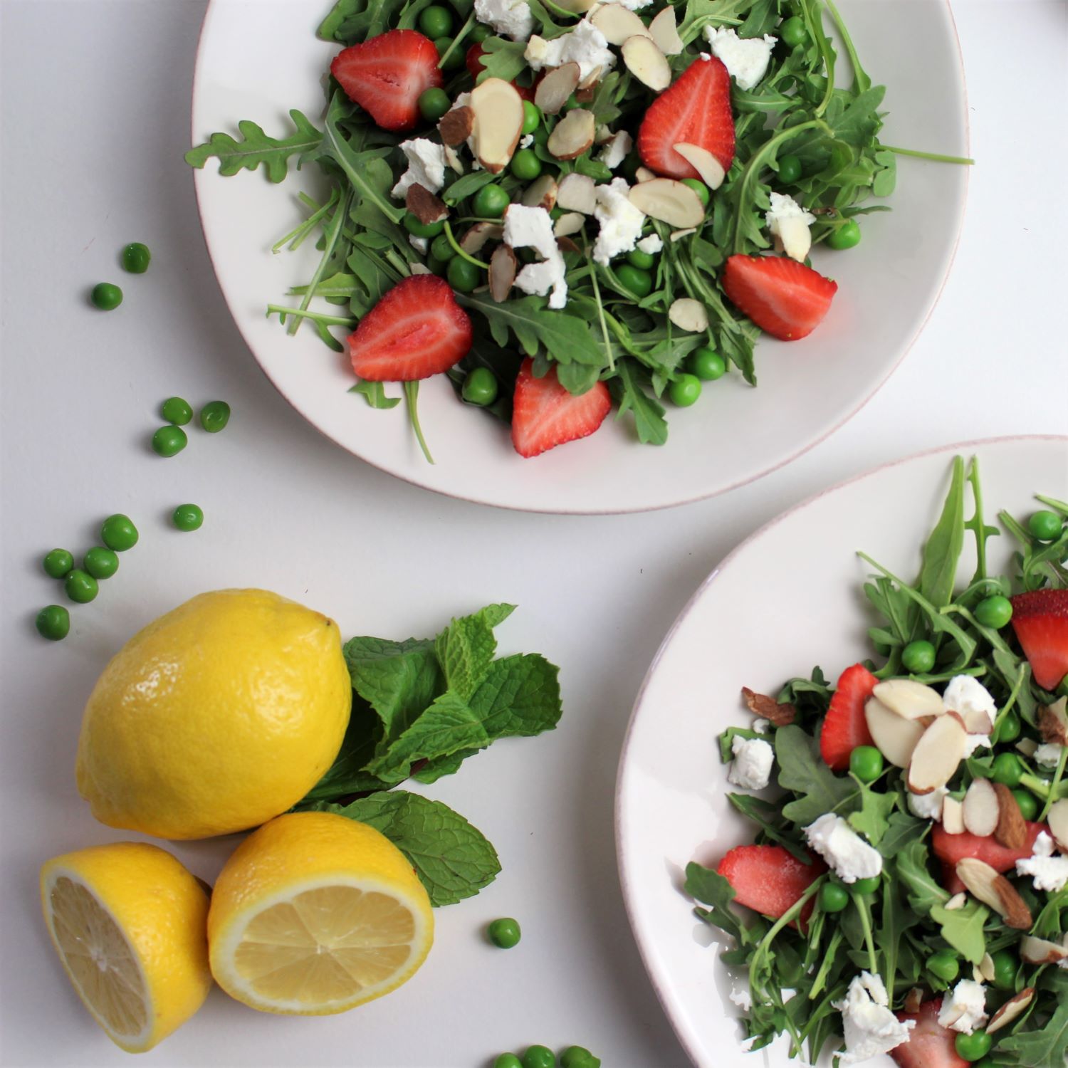 Two plates of easy peasy arugula salad with a lmeon on the side.