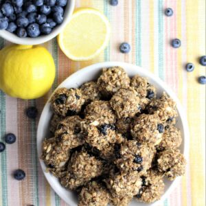 Lemon Blueberry Energy Balls in a bowl with a sliced lemon and cup of blueberries