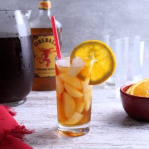 A tall glass of iced tea with a shot of fireball garnished with an orange wheel slice.