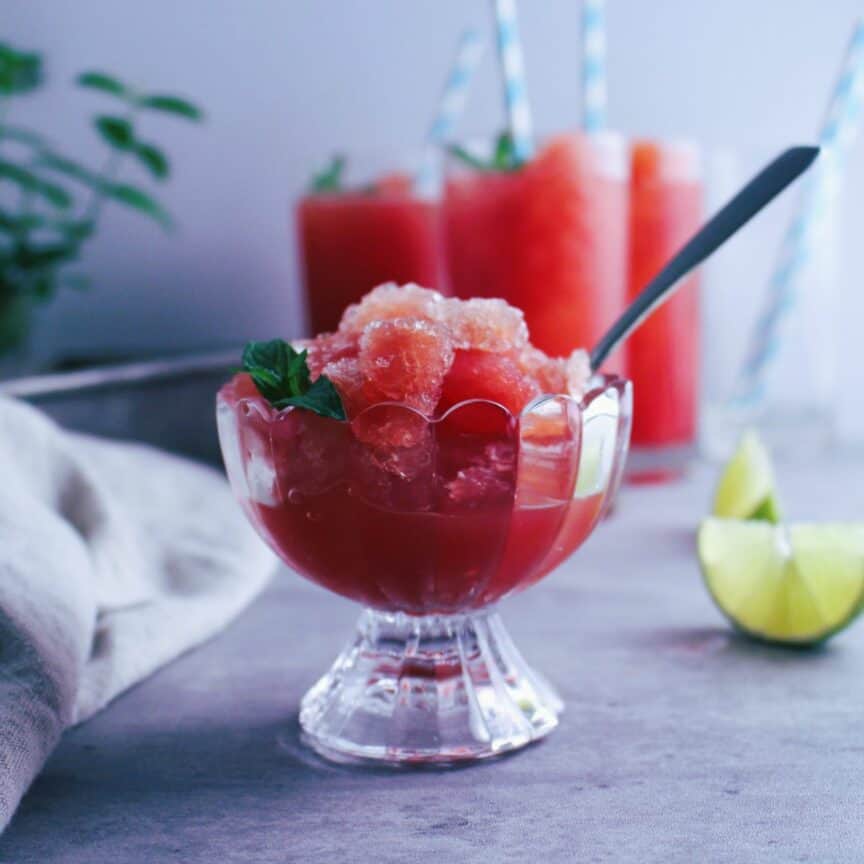Watermelon mint granita scooped into a footed glass dish with a sprig of mint.